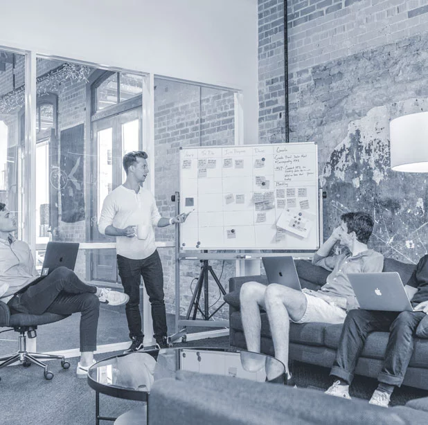 A group of people sitting around a whiteboard as the presenter goes over a userflow plan and notes