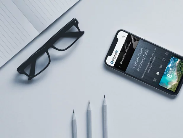 Overhead view of a notepad, pencils, eye glasses and a phone with the DigitalB website shown